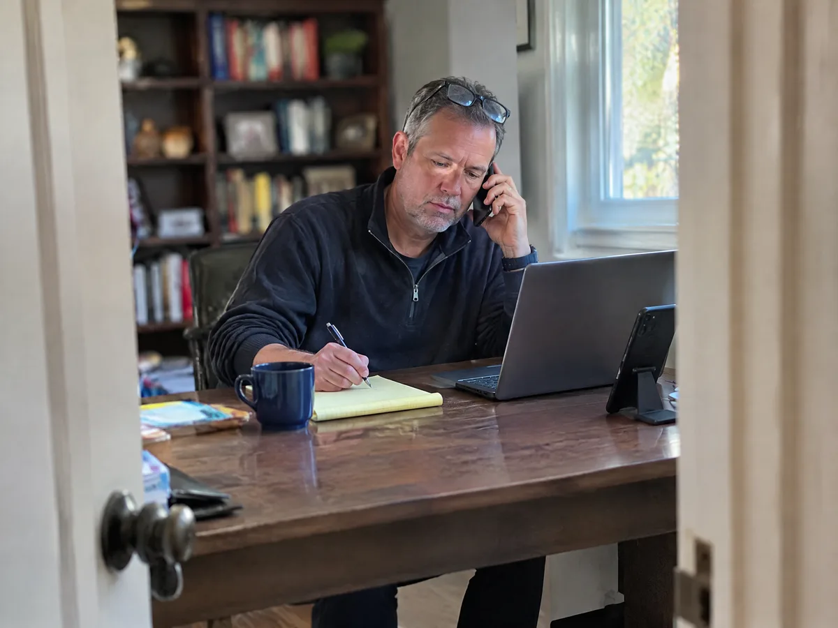 A business coach taking notes during a call in his home office