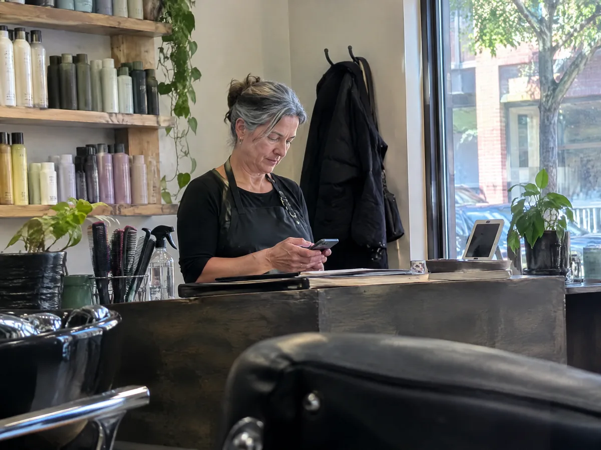 A salon owner checking her phone at the front desk between clients