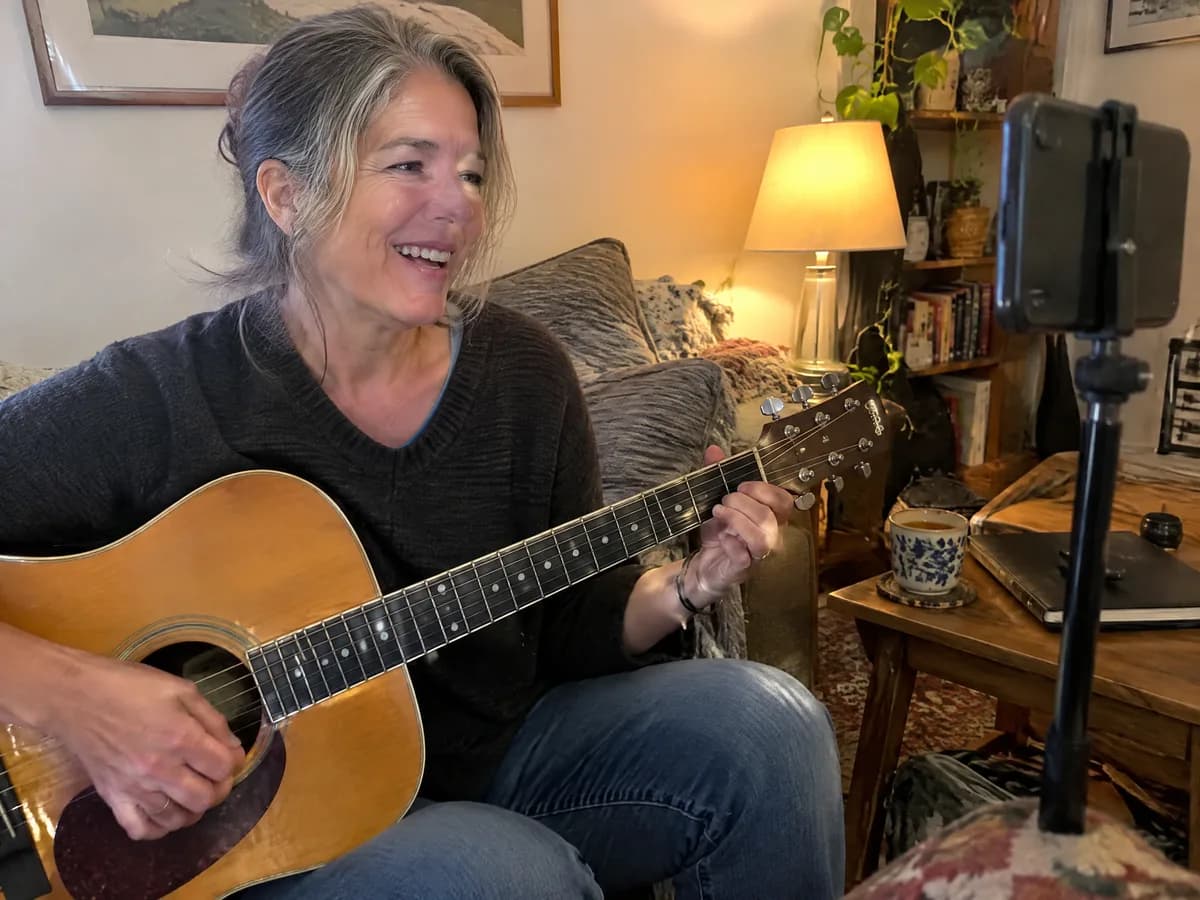 A guitar teacher recording a lesson in her living room